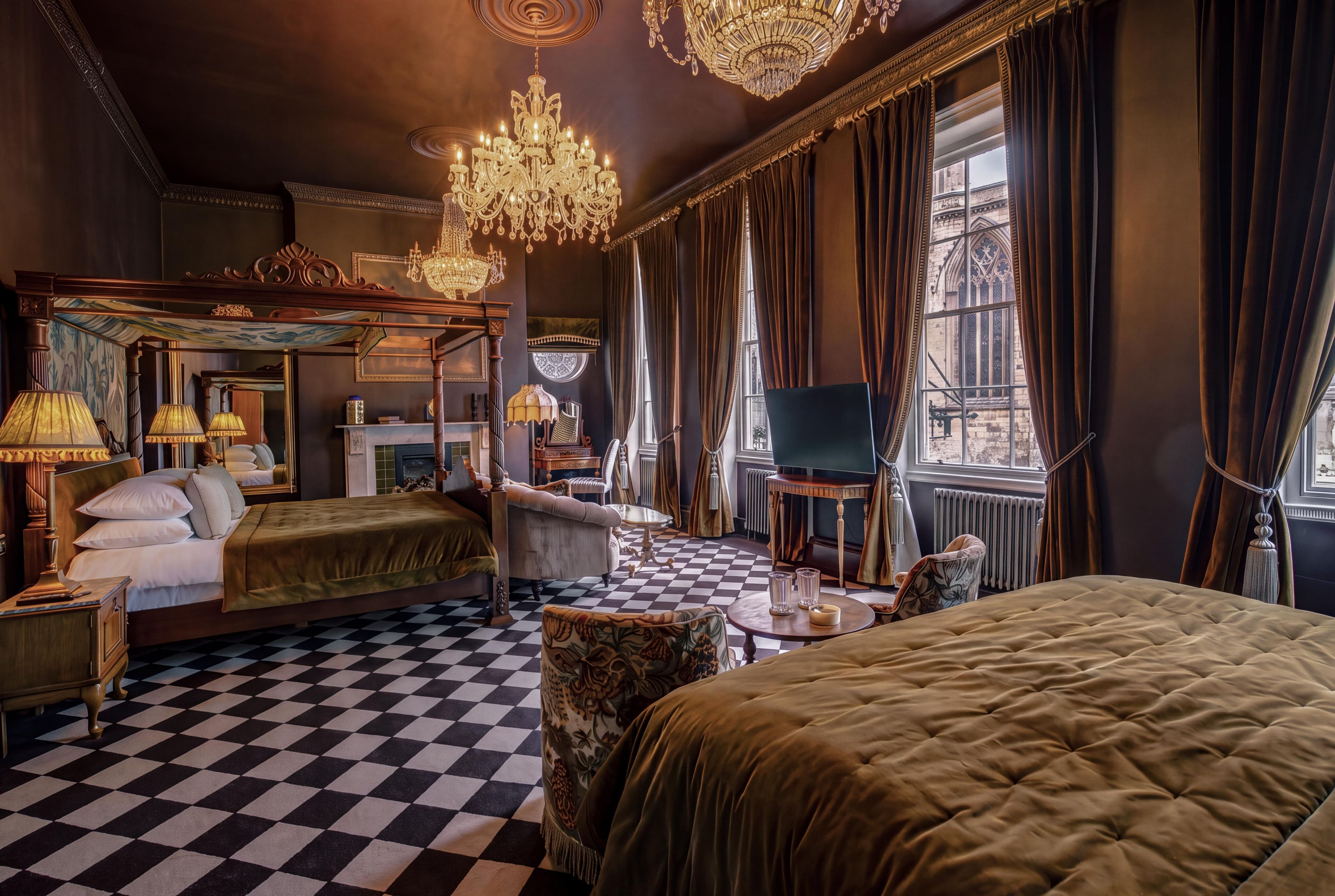 Ein Hotelzimmer mit Schachbrettmuster-Boden, einem Himmelbett, einem Fernseher und einem Kamin.