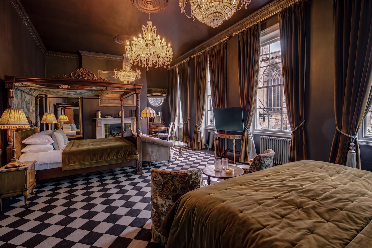 A hotel room with a checkered floor, a four-poster bed, a television, and a fireplace.