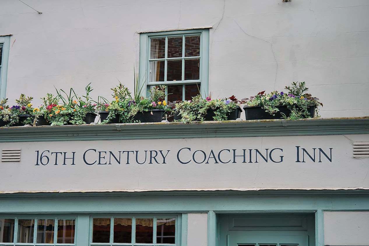 A building with a sign reading '16th Century Coaching Inn' and flower boxes on the roof.