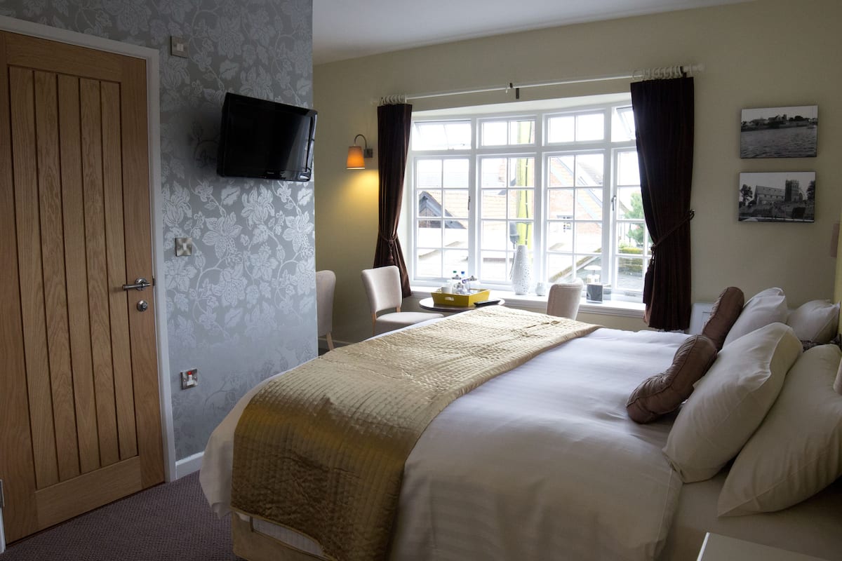 Una habitación de hotel con cama, televisión, ventana con cortinas y vistas al exterior.
