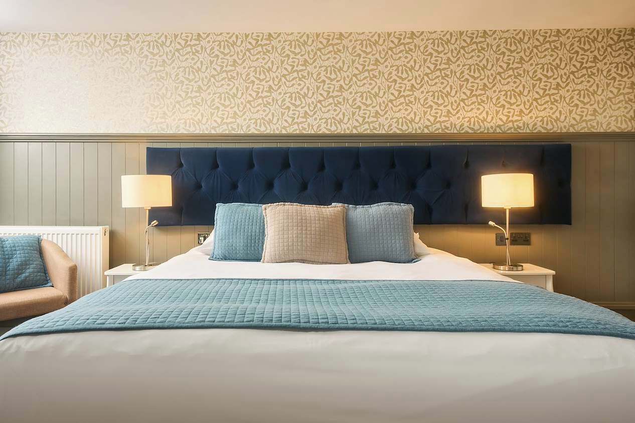 Une chambre d’hôtel avec un grand lit, deux lampes de chevet, un mur à motifs et une chaise.