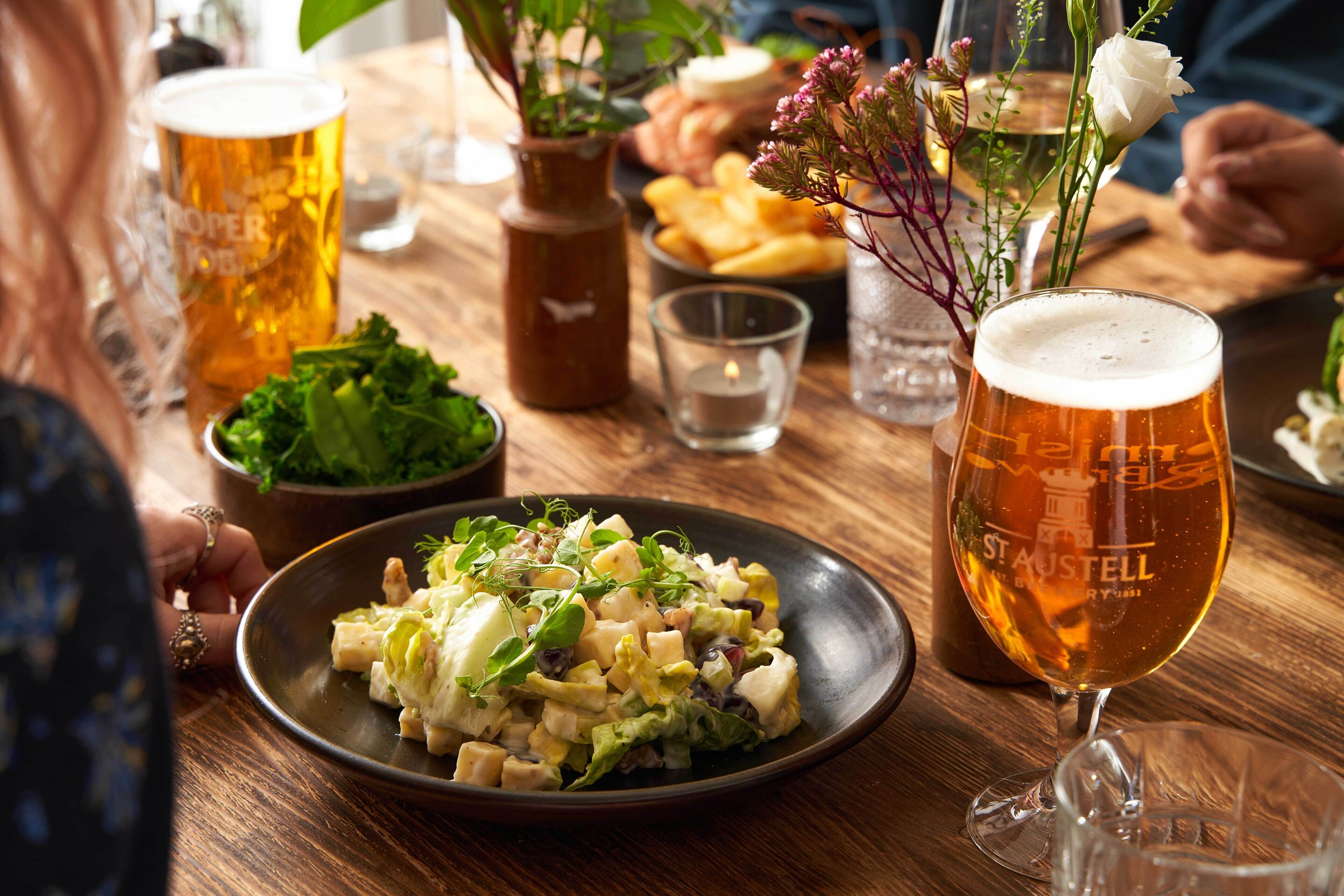 A wooden table with a plate of food, a glass of beer, and a candle.