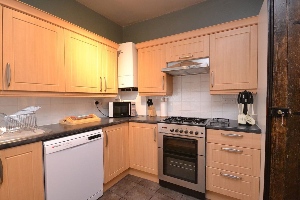 Una cocina moderna con armarios de madera, lavavajillas, microondas, estufa y pileta.