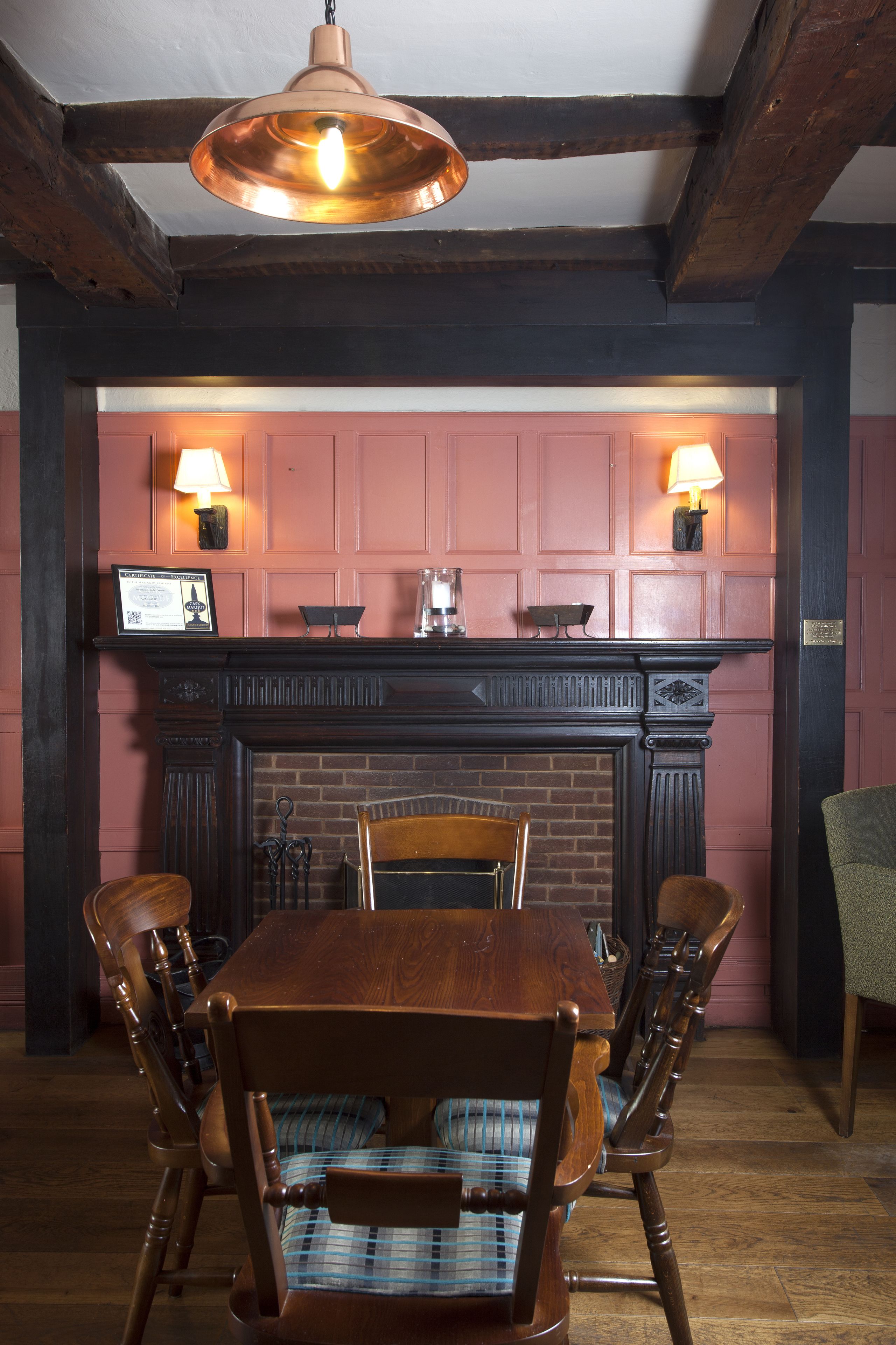 A dining area with a wooden table and chairs, a brick fireplace, and two wall-mounted lamps.