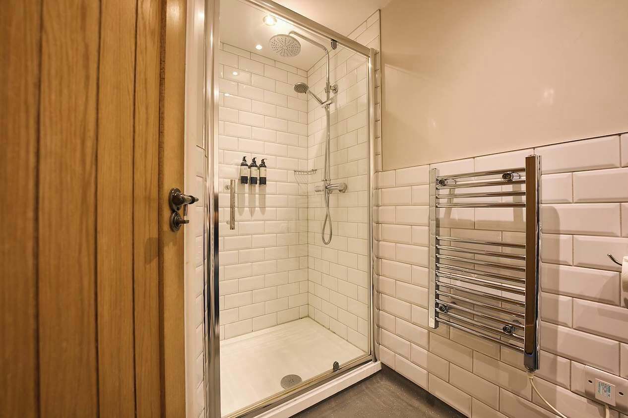 A glass-enclosed shower with a handheld showerhead and a wall-mounted towel rack.