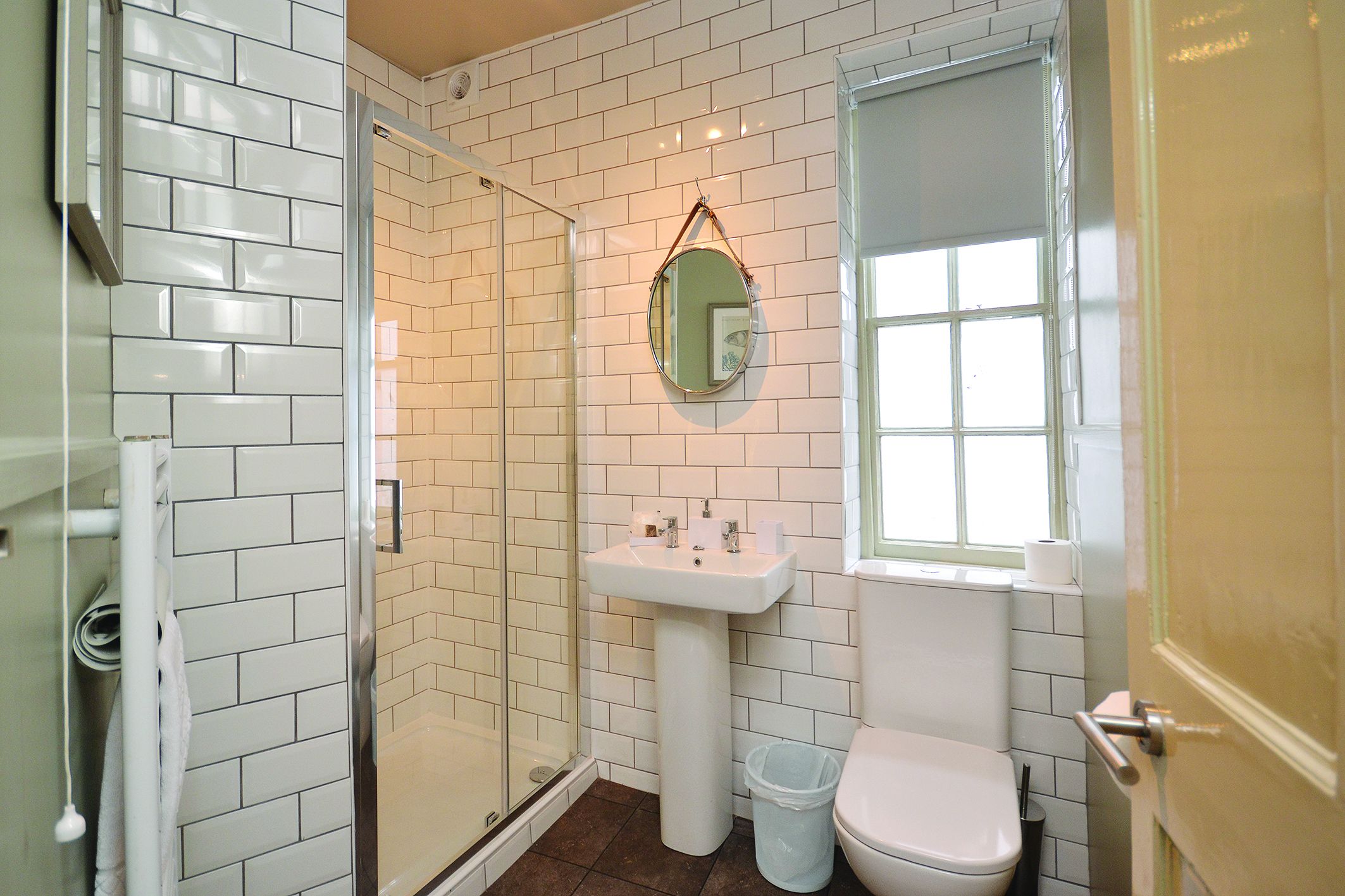 Un baño con paredes de azulejos blancos, un lavabo con pedestal, un inodoro y una cabina de ducha de vidrio.