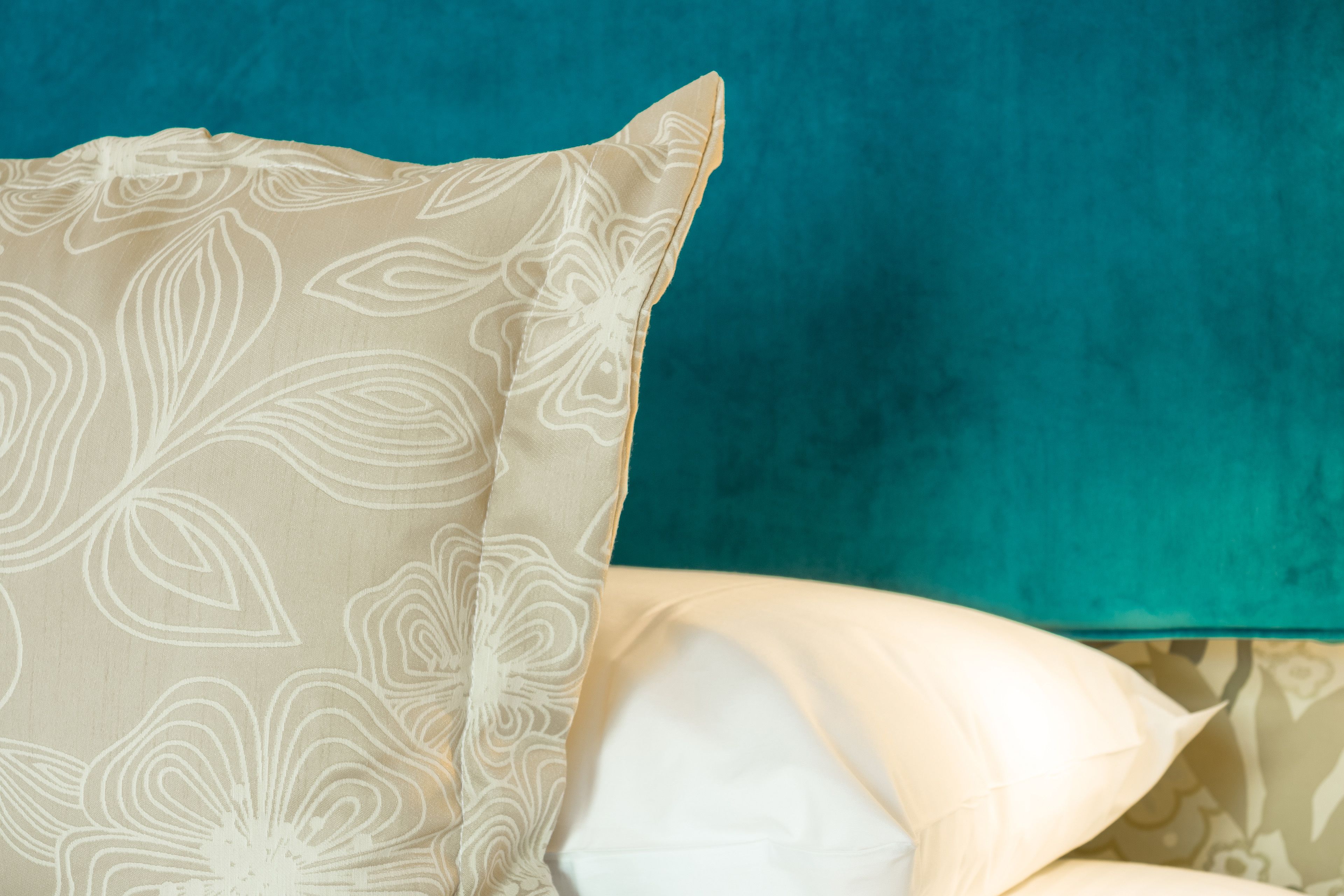A bed with a patterned pillow and a teal-colored headboard.