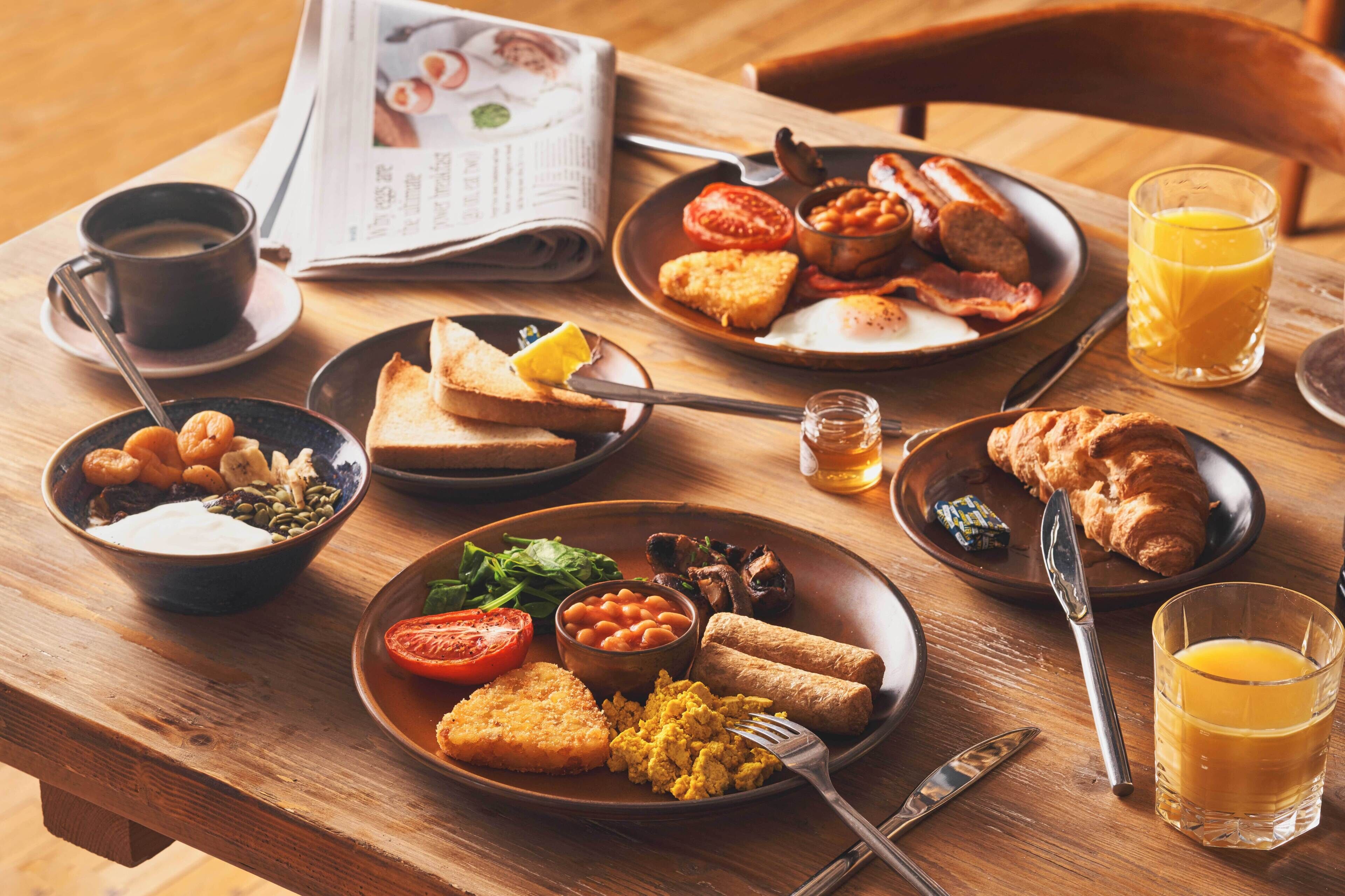 A breakfast table with various dishes, a newspaper, and a glass of orange juice.