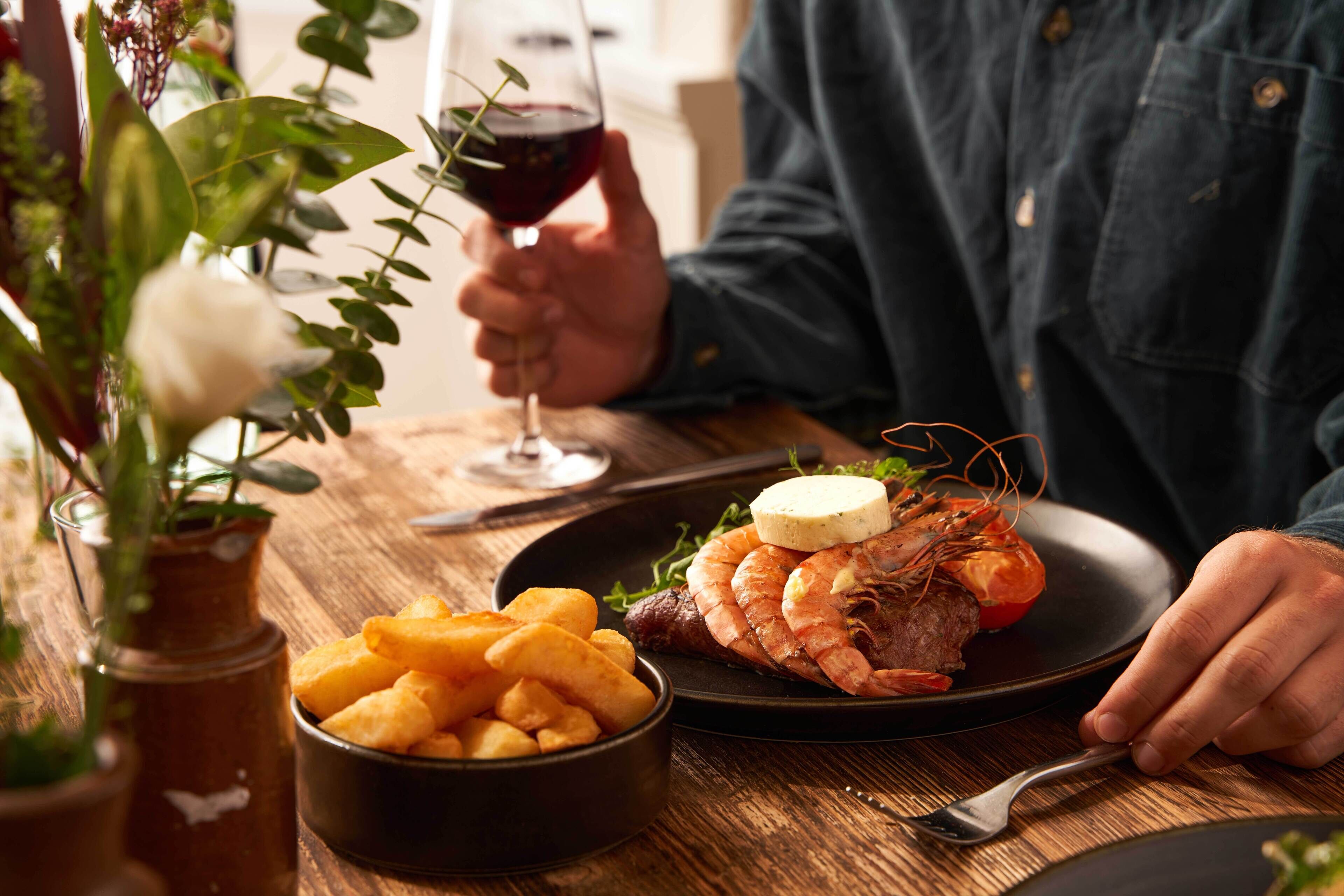 Une table à manger avec une assiette de nourriture, un verre de vin rouge et un bol de frites.