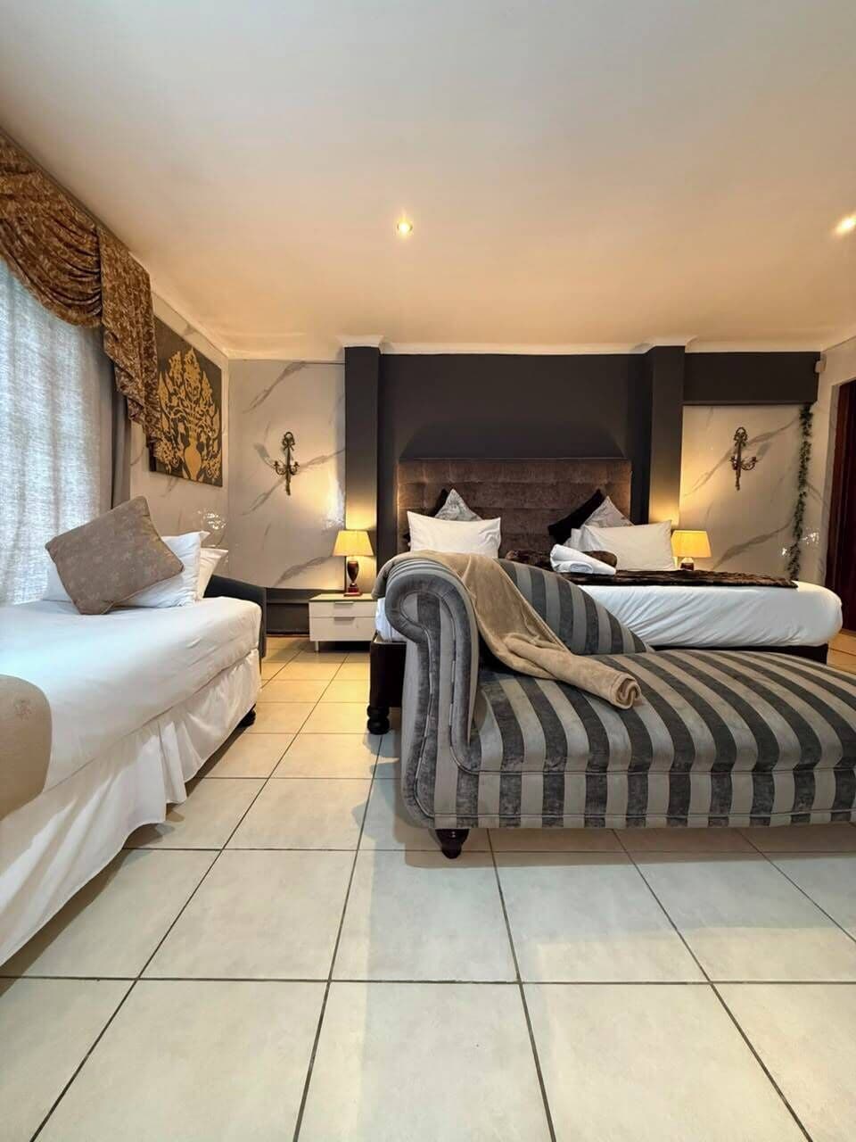 A hotel room with a bed, a sofa, a nightstand, and a wall-mounted lamp.