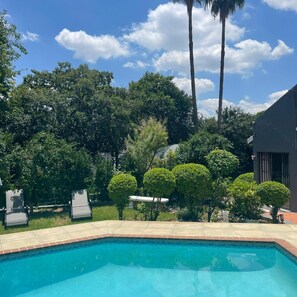 A swimming pool surrounded by lush greenery and a modern building. - Marion Lodge (Sandton)