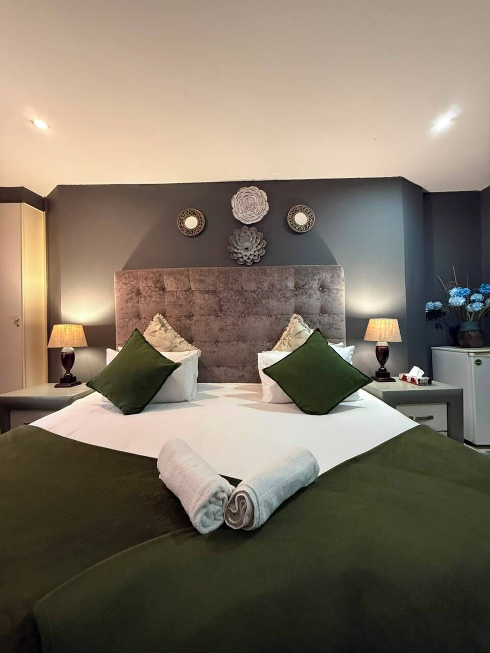 Een moderne slaapkamer met een groot bed, twee nachtkastjes en decoratieve wanddecoratie.