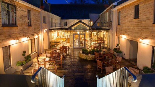 A courtyard with wooden buildings, outdoor seating, and a glass entrance.