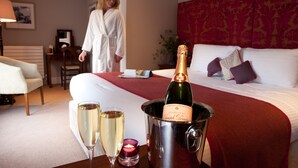 A hotel room with a bed, a bedside table with a bottle of champagne, two glasses of champagne, and a lit candle.