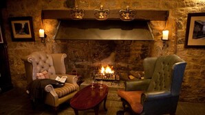 A cozy room with a stone fireplace, two upholstered chairs, a wooden coffee table, and wall-mounted sconces.