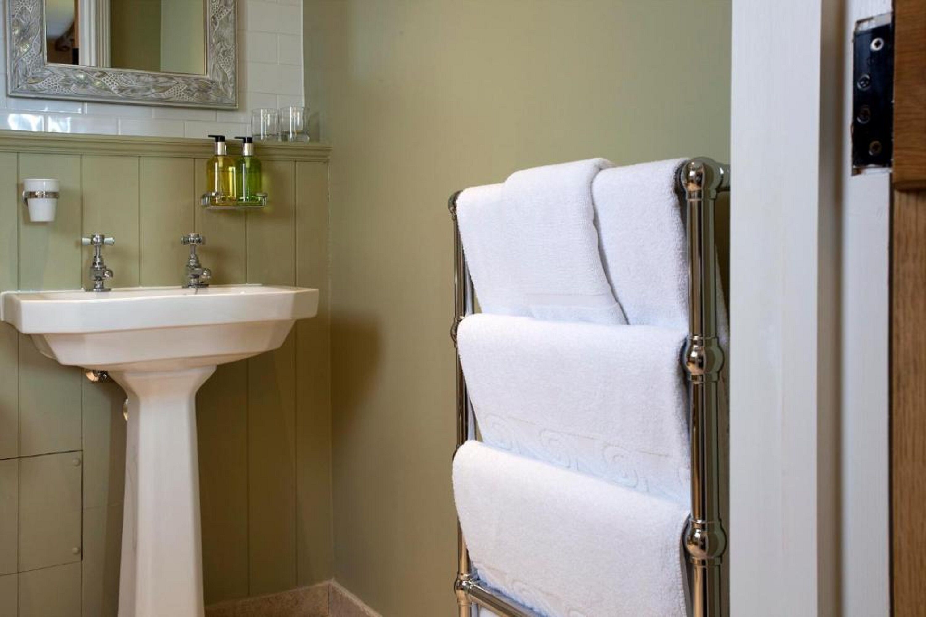 A bathroom with a pedestal sink, a mirror, and a towel rack with towels.