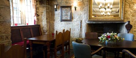 A stone-walled room with a fireplace, a dining table with chairs, and a chandelier.