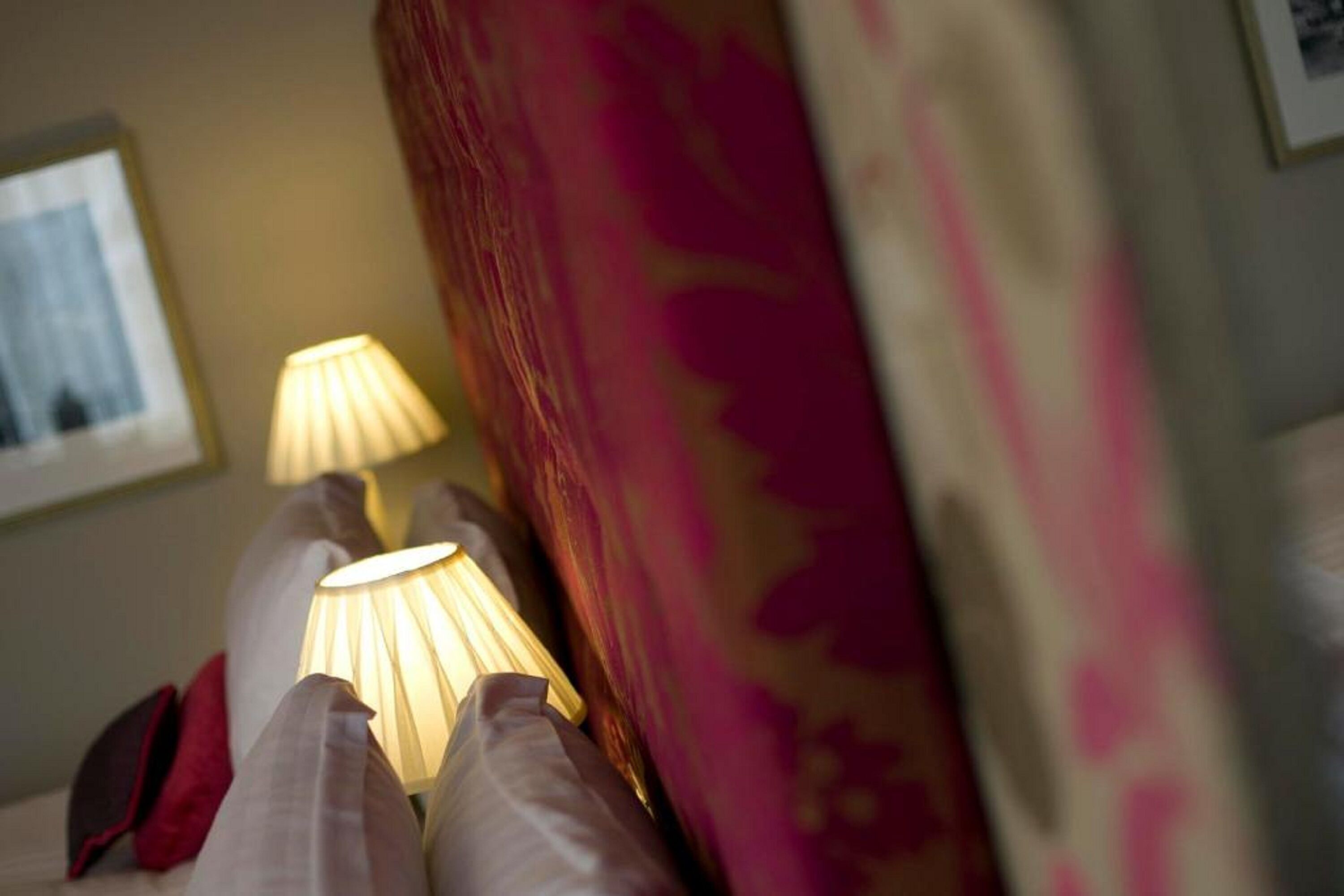 Una cama con lámpara y almohadas, un papel tapiz estampado y un cuadro enmarcado.