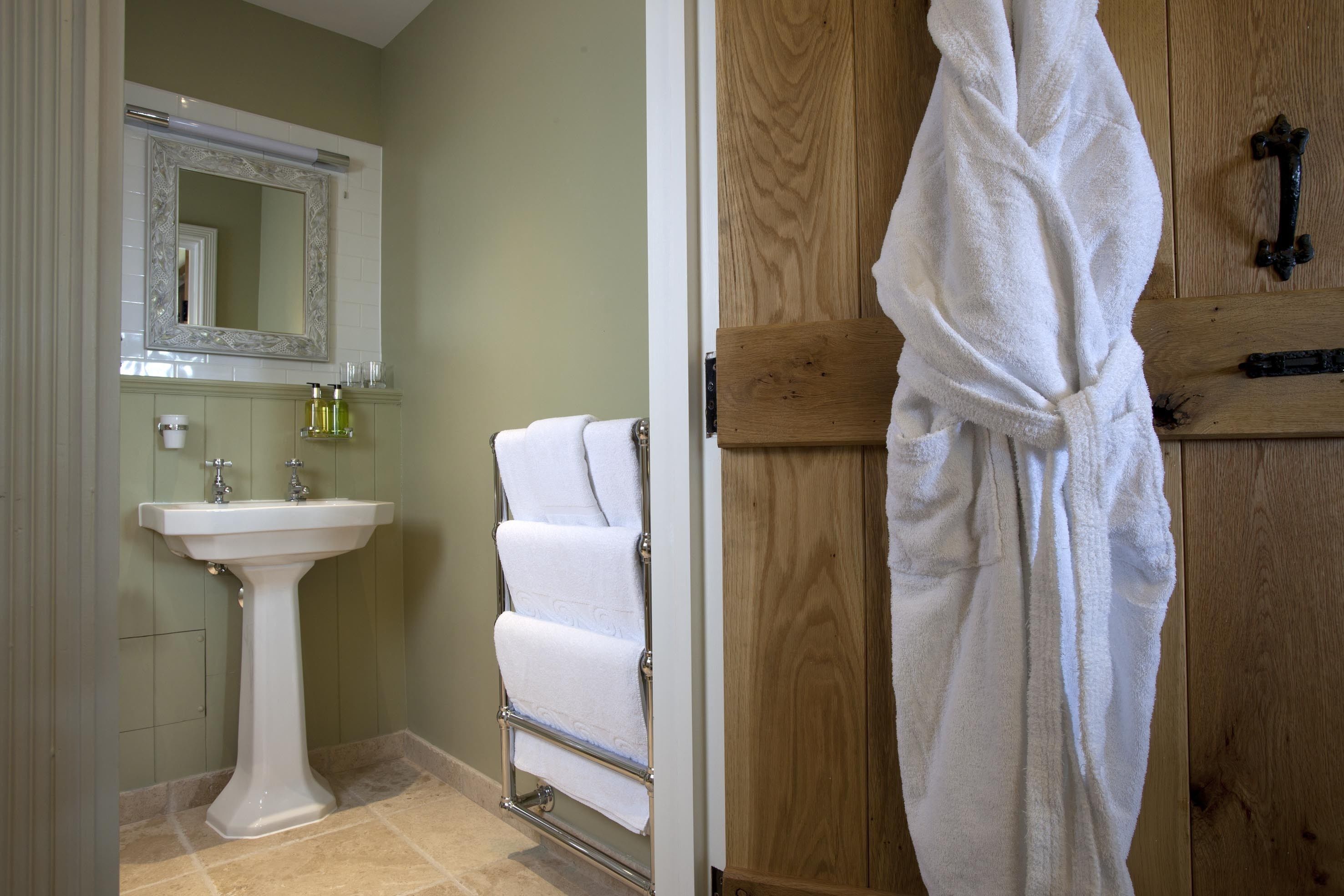 Une salle de bain avec un lavabo sur pied, un porte-serviettes et une porte en bois sur laquelle est accroché un peignoir.