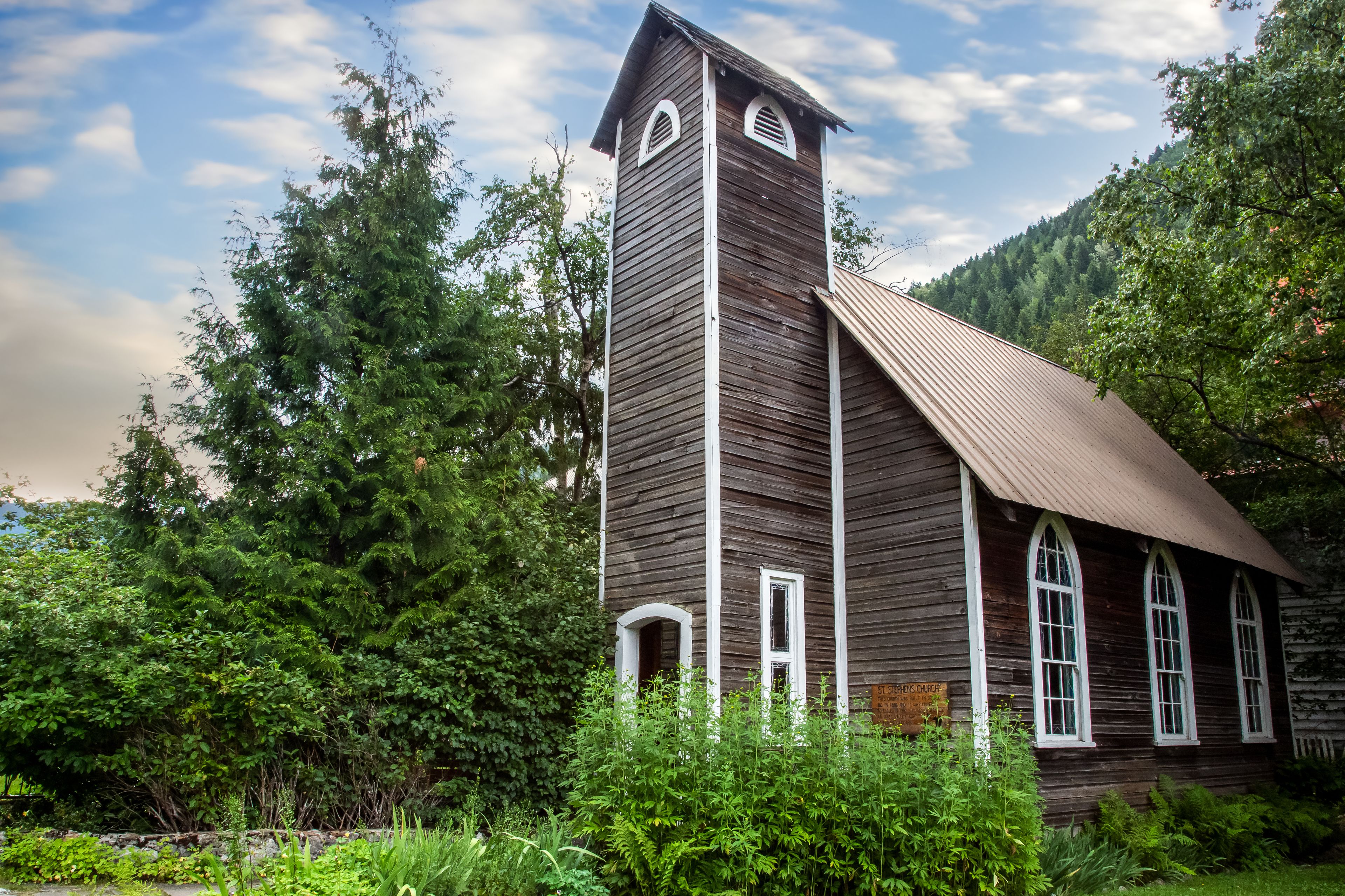 Une église en bois, dotée d’un clocher, entourée d’une végétation luxuriante et d’arbres.