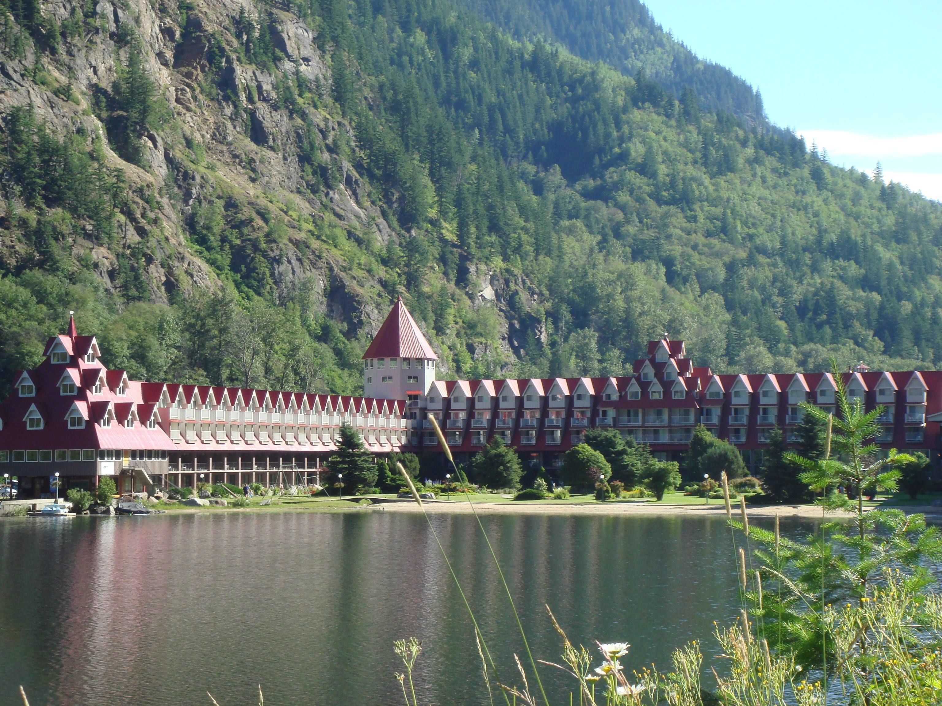 Un hôtel avec un long bâtiment longeant un lac, entouré de collines boisées.