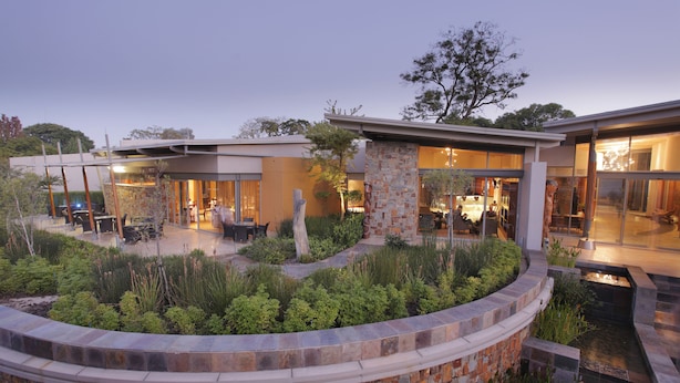 Una casa moderna con patio, muros de piedra y un pequeño elemento acuático.
