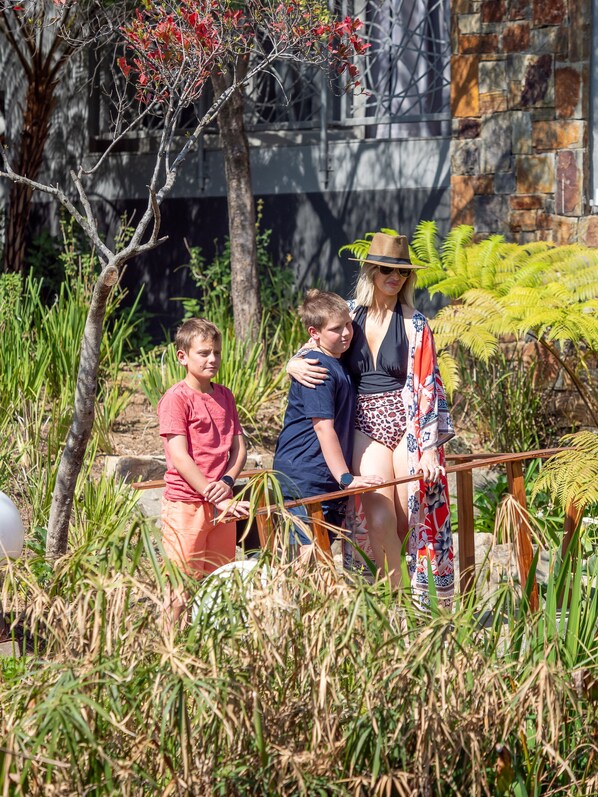 A family standing by a wooden railing in a garden with trees and ferns.