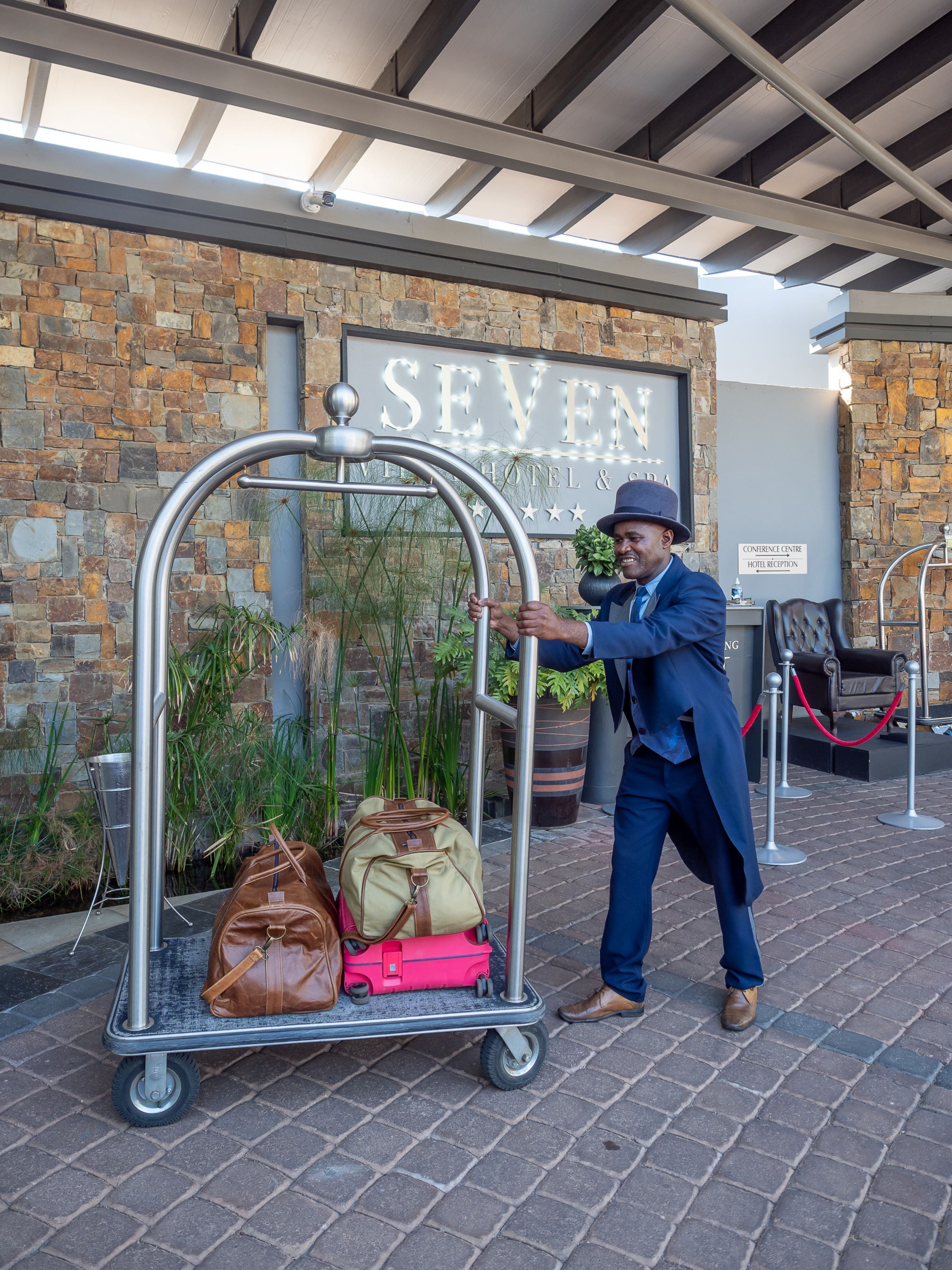 A man pushing a luggage cart outside a hotel named "SEVEN".