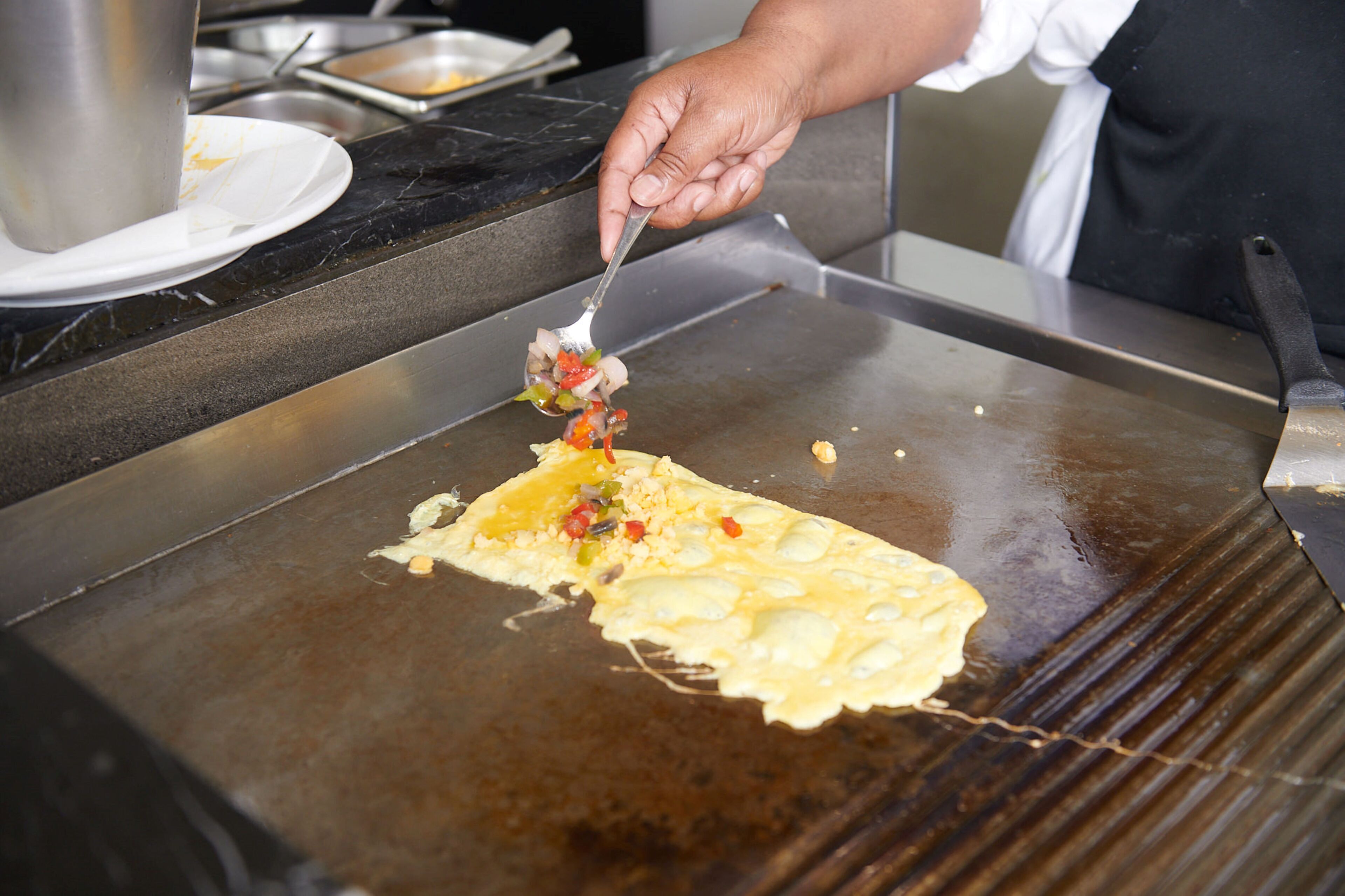 A person cooking on a large flat griddle, likely preparing a pancake or omelette.