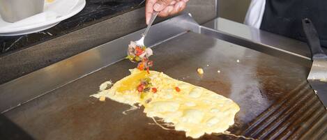 A person cooking on a large flat griddle, likely preparing a pancake or omelette.