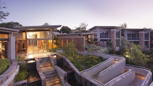 Un moderno complejo residencial con varias casas, grandes ventanales, fachadas de piedra y ladrillo, y un jardín ajardinado con fuente.