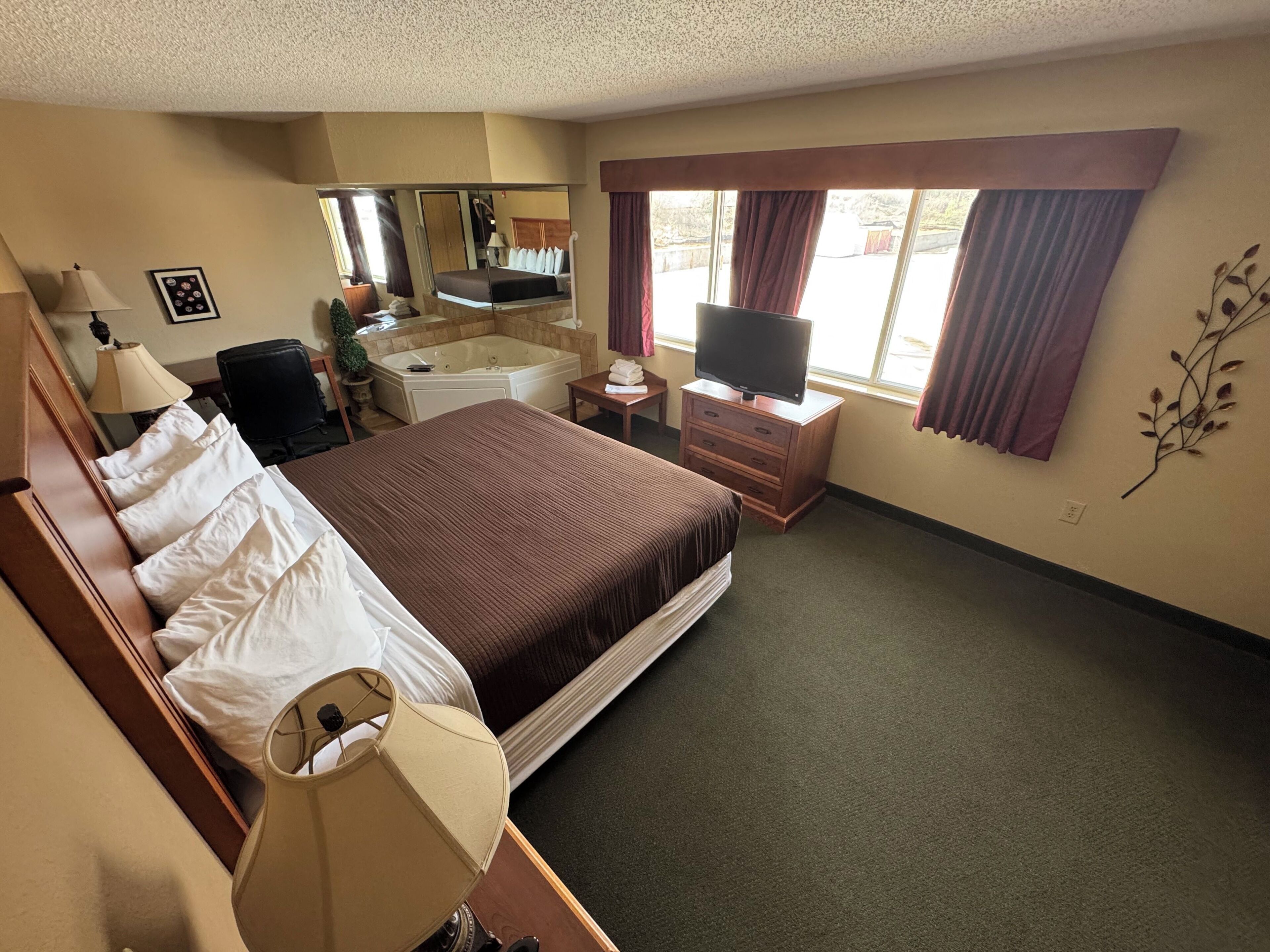 Une chambre d’hôtel avec un grand lit, un bureau, une chaise, une télévision, une salle de bain et une fenêtre avec des rideaux.
