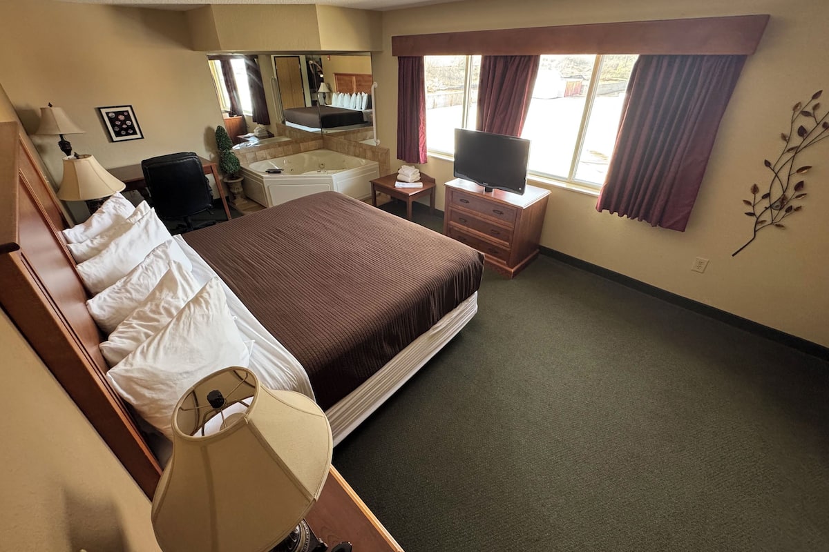 A hotel room with a large bed, a desk, a chair, a TV, a bathroom, and a window with curtains.