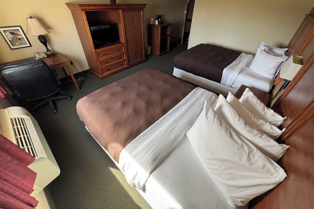 A hotel room with two beds, a desk, a television, and a cabinet.