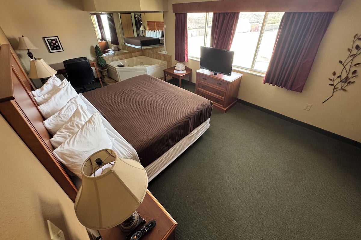 A hotel room with a bed, a TV, a desk, a lamp, a mirror, and a window with curtains.