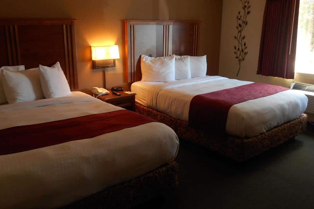 A hotel room with two beds, a bedside table with a lamp, a telephone, and a decorative wall piece.