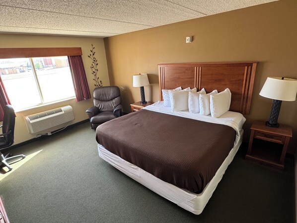 Een hotelkamer met een groot bed, twee nachtkastjes met lampen, een stoel, een raam met gordijnen en een wandairconditioner.