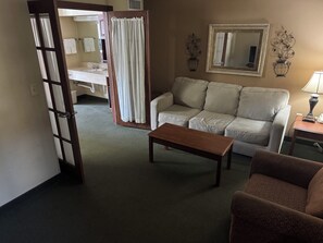 Een woonkamer met een bank, salontafel, stoel, en een badkamer met douchegordijn en spiegel.