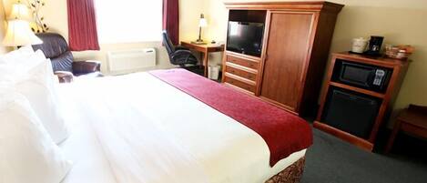 Habitación de hotel con una cama grande, un armario de madera, un escritorio con silla, televisor y microondas.