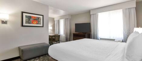 Habitación de hotel con una cama grande, un escritorio con silla, un televisor y una ventana con cortinas.