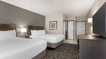 A hotel room with two beds, a desk, a TV, a lamp, and a painting on the wall.