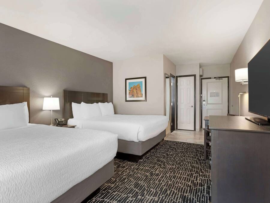 A hotel room with two beds, a desk, a TV, a lamp, and a painting on the wall.