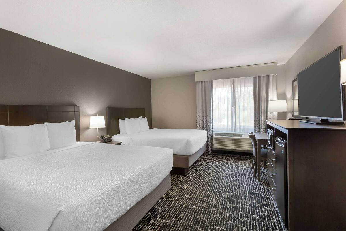 Ein Hotelzimmer mit zwei Betten, einem Schreibtisch mit Fernseher und einem Fenster mit Vorhängen.
