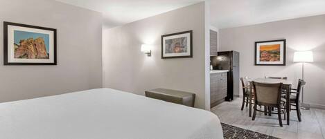 A hotel room with a bed, a desk with a chair, a small bench, and framed pictures on the walls.
