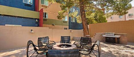 An outdoor patio with a fire pit, seating, and a grill.