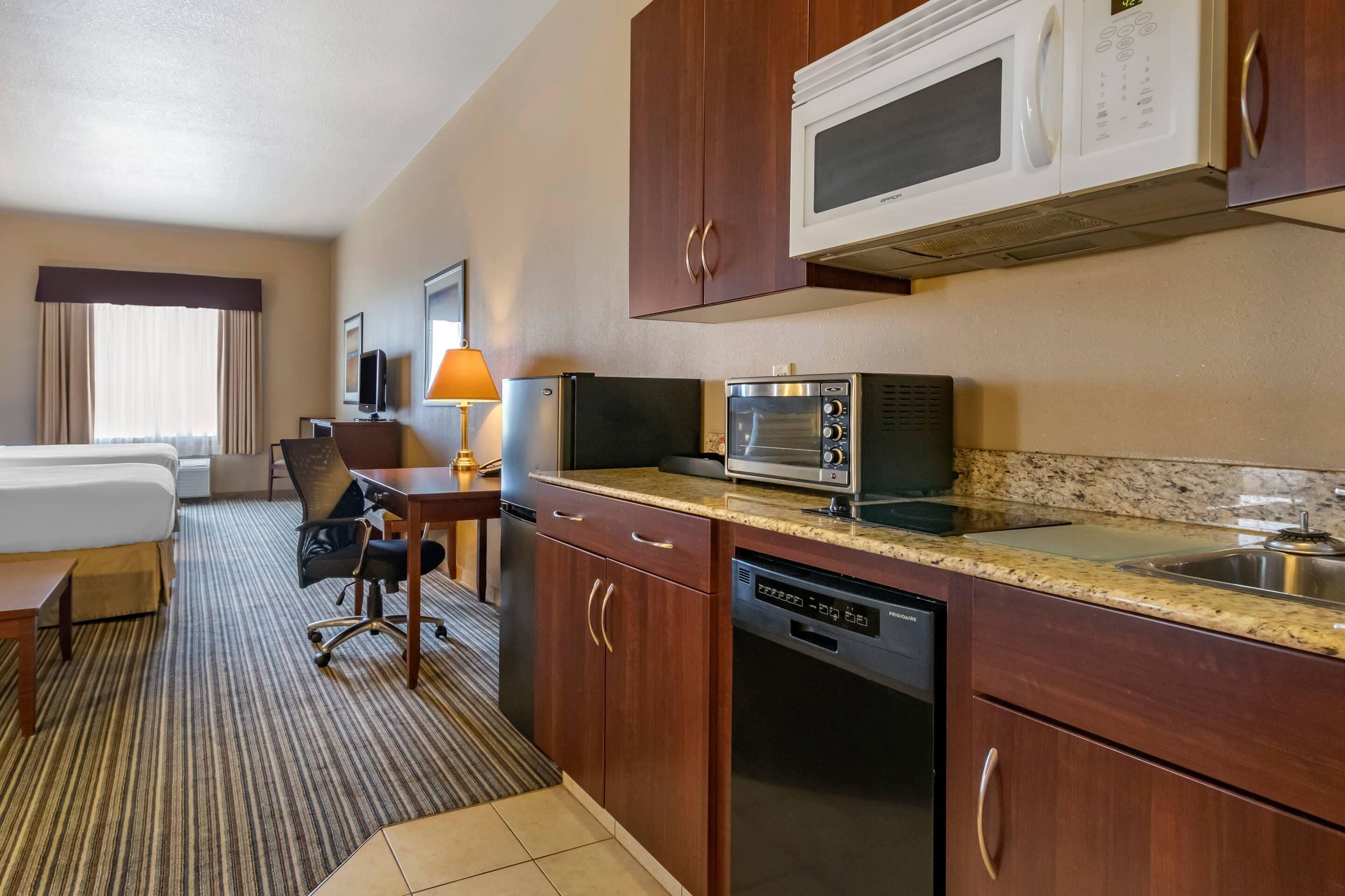 Habitación de hotel con kitchenette que incluye microondas, tostadora y lavavajillas. Cuenta con una cama, un escritorio con lámpara y una silla.