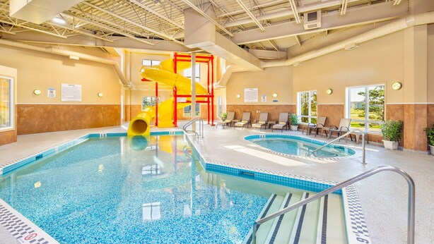 An indoor swimming pool with two lanes, a yellow slide, and lounge chairs by the windows. - Quality Inn & Suites Rimbey (Rimbey)