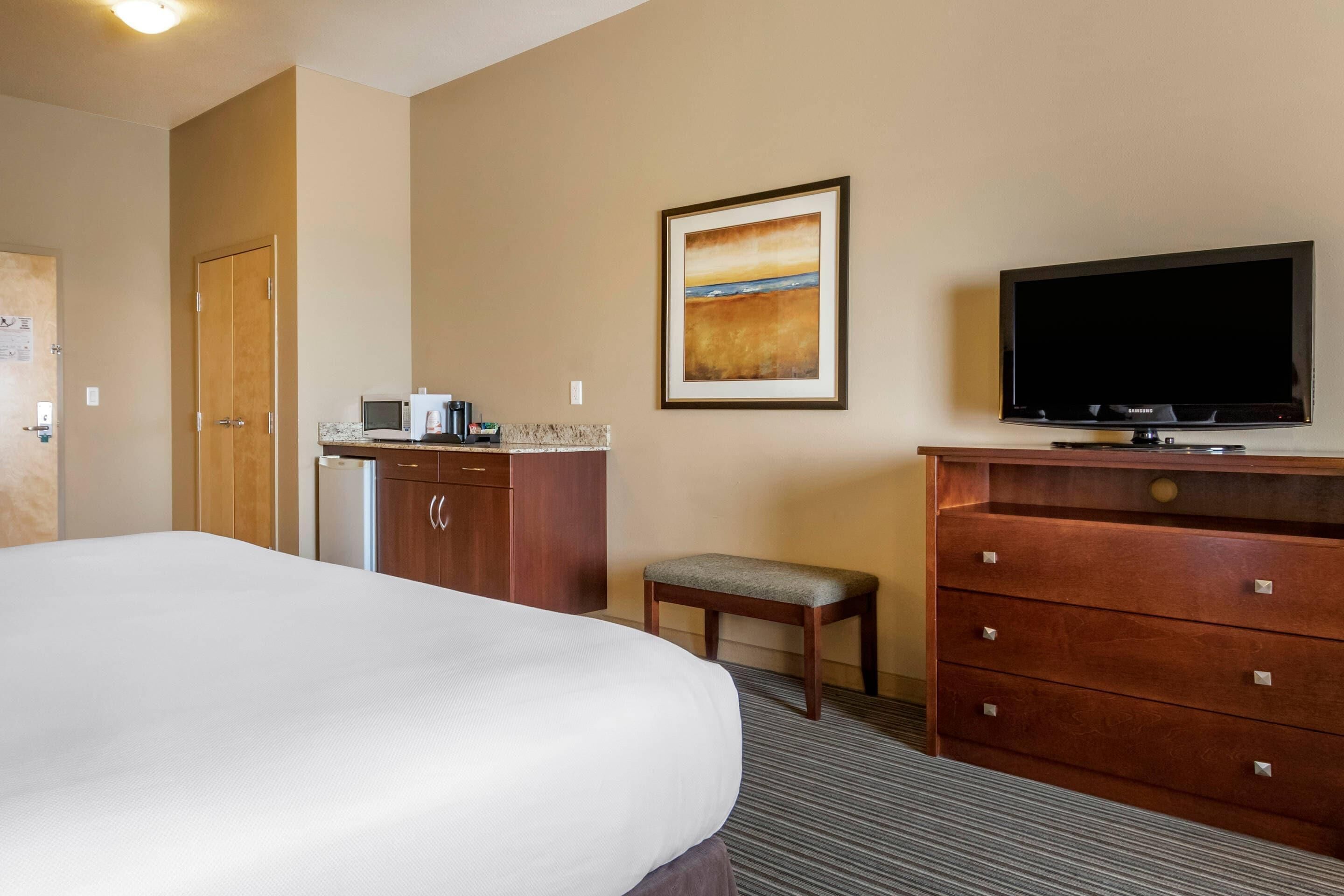 A hotel room with a bed, a television, a desk with a computer, a chair, and a cabinet.