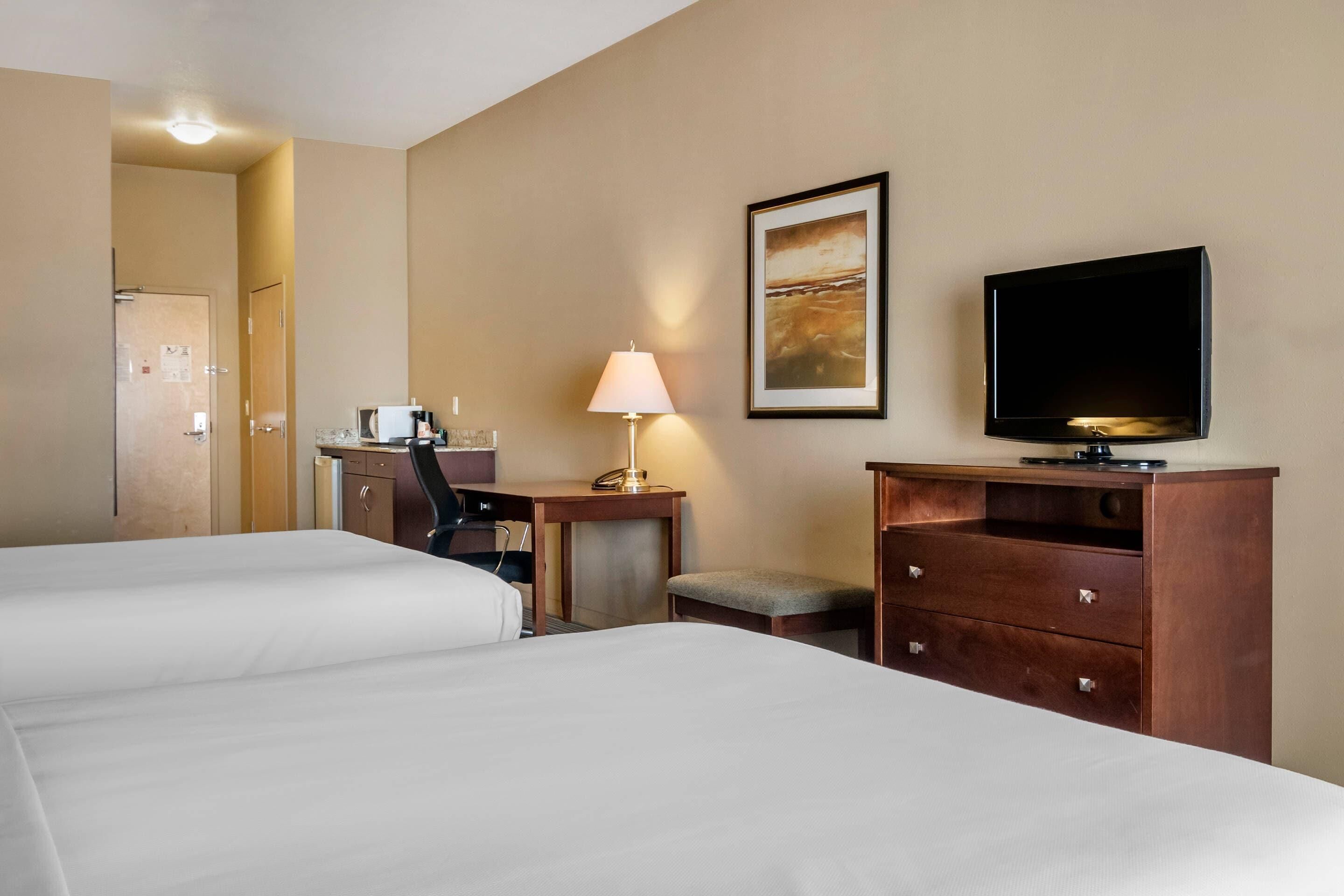 Ein Hotelzimmer mit zwei Betten, einem Schreibtisch mit Lampe, einem Fernseher und einem gerahmten Bild an der Wand.