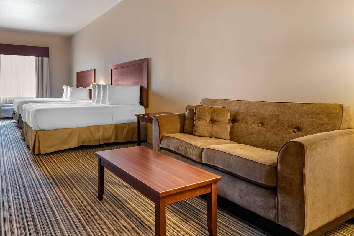 A hotel room with two beds, a sofa, a wooden table, and a window with curtains.